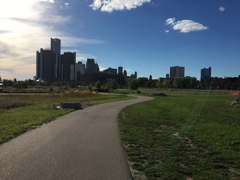 The RiverWalk path winding through William G. Milliken State Park, with the Renaissance Center and downtown behind (2018)