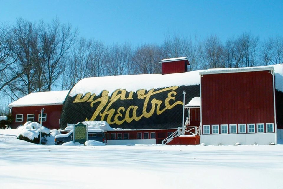 A Barn Theatre vörös pajtaépülete hóban, a tetőn nagy arany Barn Theatre felirattal, kék ég alatt