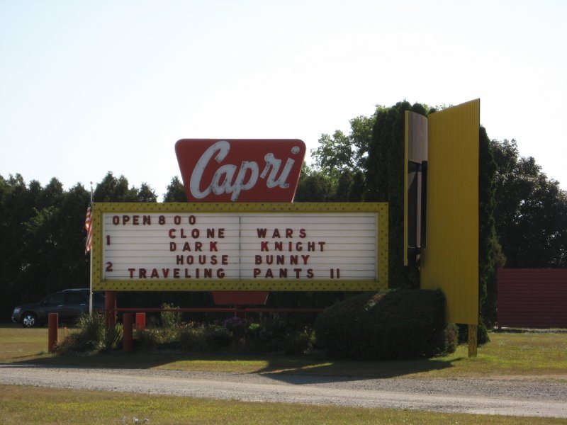 The Capri Drive-In's red Capri sign and letterboard listing the double features, by the road in daylight