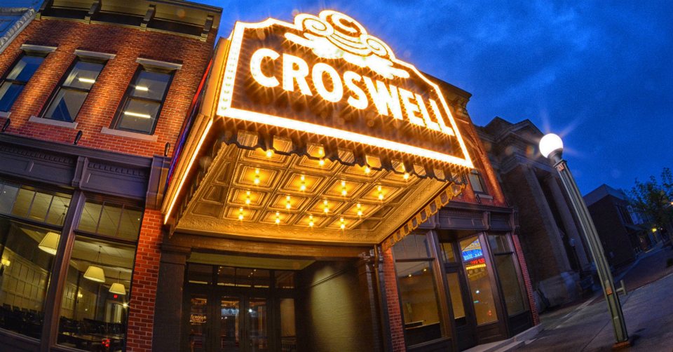 The Croswell's glowing golden marquee and coffered entrance canopy under a blue evening sky
