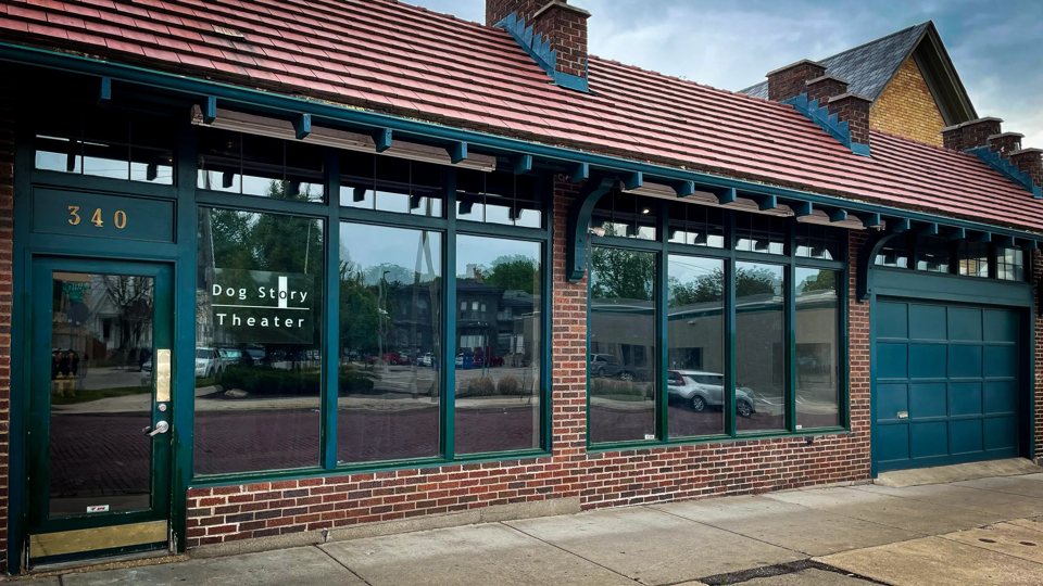 The Dog Story Theater sign in the green-framed storefront windows of the red-tile-roofed brick building at number 340