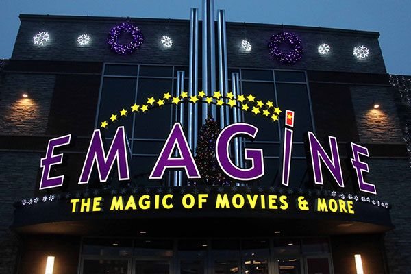 Az Emagine lila betűi, csillagíve és sárga „The Magic of Movies & More” felirata alkonyatkor, ünnepi díszekkel a homlokzaton