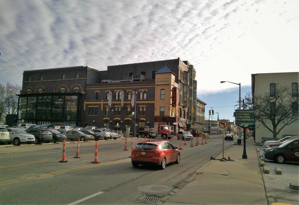 A Grand Rapids Civic Theatre téglaépülete függőleges piros felirattal a belvárosi utcán, előtte parkoló autók és terelőbóják