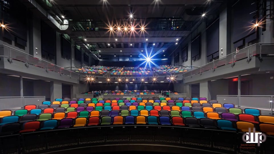The renovated auditorium with multicoloured seats, two balconies and sparkling lights, seen from the stage