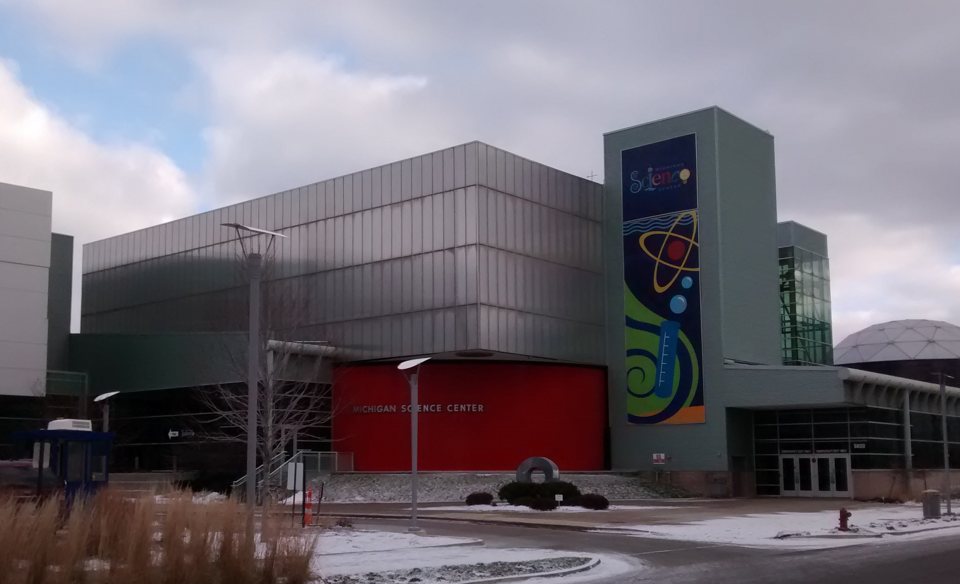 A Michigan Science Center épülete piros bejárati fallal, színes zászlóval és a jobb szélen a kupolával, havas téli napon