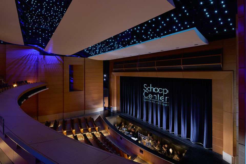 The Schaap Center auditorium seen from the balcony, with wood panelling, a starry lit ceiling, the orchestra pit and a blue curtain
