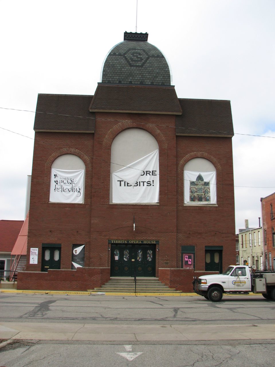 The opera house's simplified brick facade with its dome and Restore Tibbits! banners in the arched windows