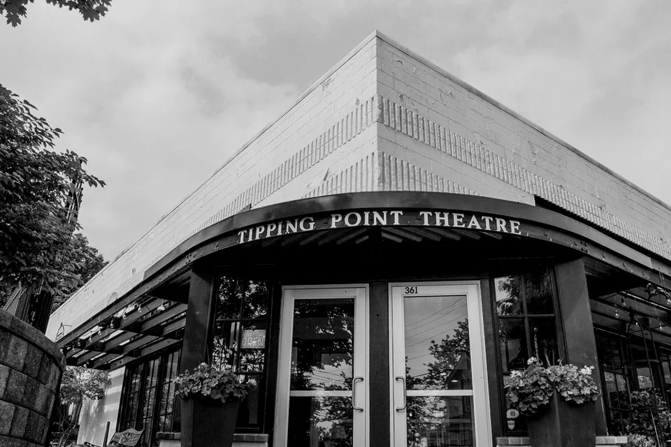A Tipping Point Theatre íves feliratú saroki bejárata virágládákkal, fekete-fehérben