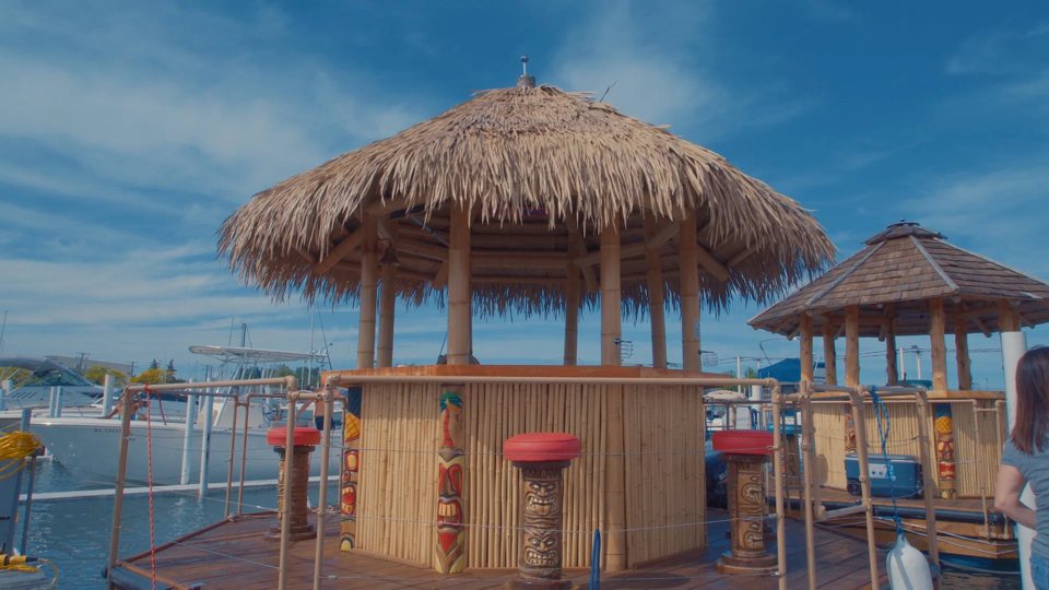 Thatched-roof tiki bar boats docked at the marina with sailboats behind them