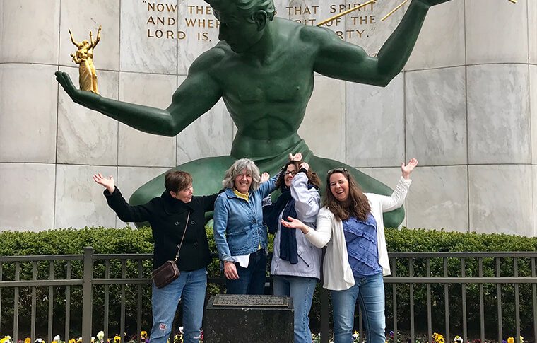 A group of four wave for a photo in front of the Spirit of Detroit statue