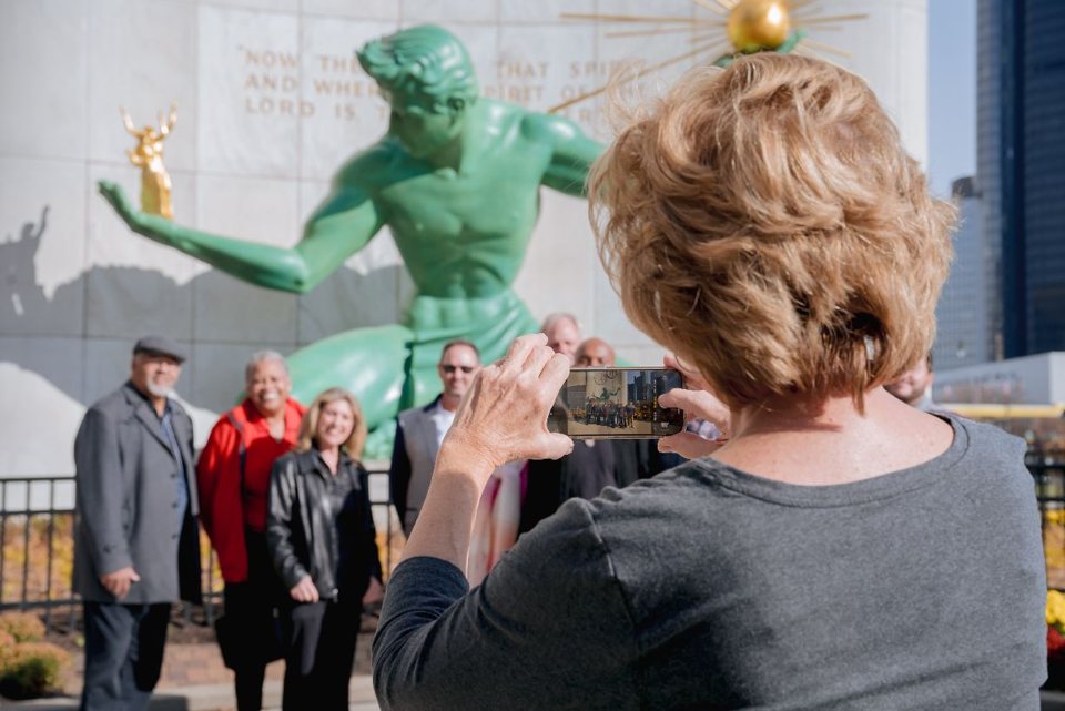 A woman photographs the tour group in front of the Spirit of Detroit statue