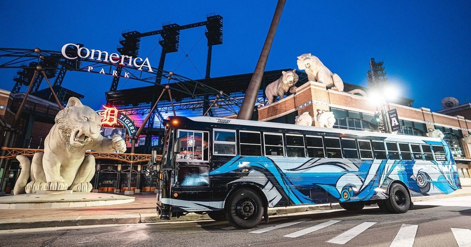 A cég festett busza a Comerica Park előtt áll éjszaka, a tigrisszobrokkal