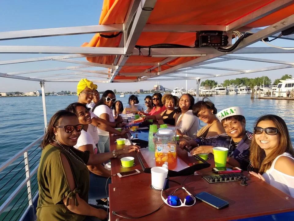 A festive group celebrates aboard the Detroit Cycle Boat, with the marina behind them