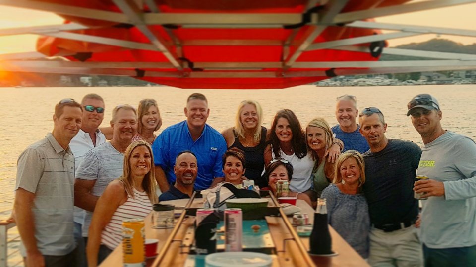 A large group poses at sunset on the bar boat, with the marina in the background