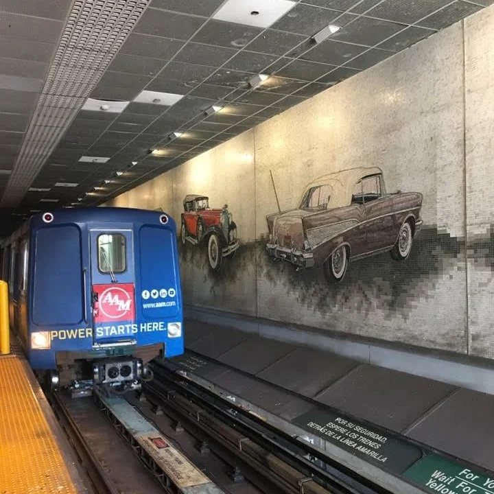 A People Mover szerelvénye egy belvárosi állomáson, a falon régi autókat ábrázoló falfestmény
