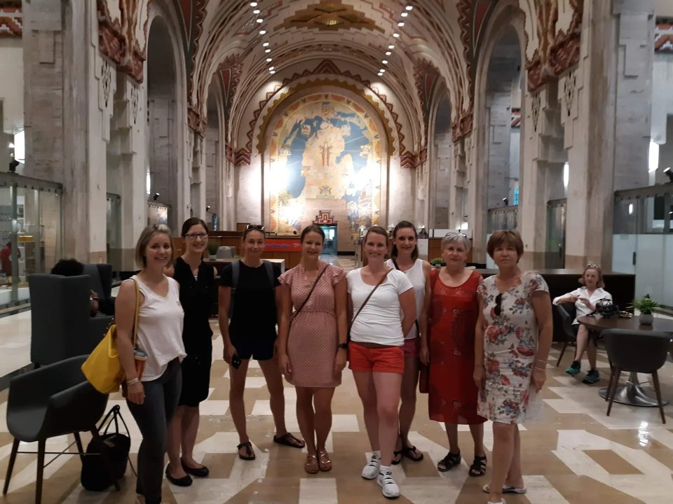 A group of eight women stands in the ornately painted, arched lobby of the Guardian Building