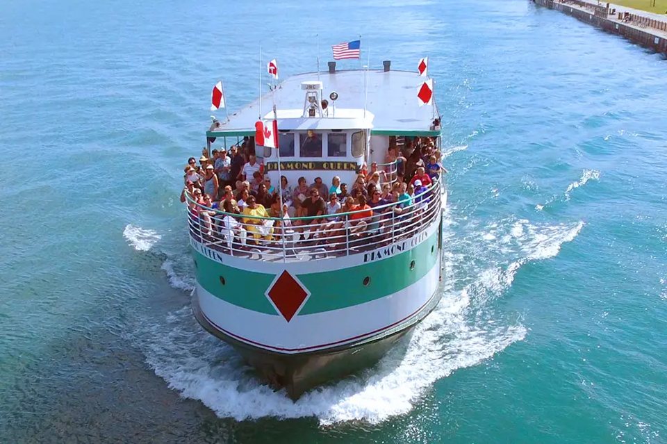 A sightseeing boat full of passengers cutting across the Detroit River