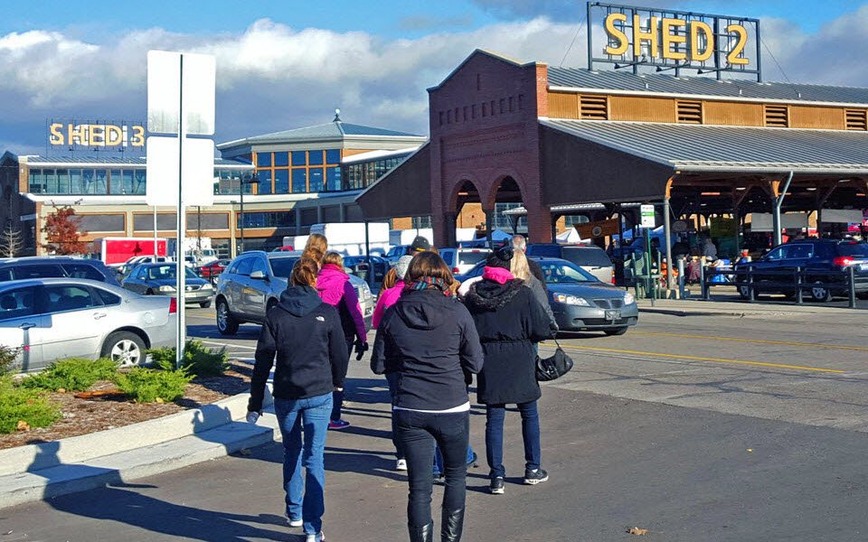 A group walks toward the Eastern Market Shed 2 building across the parking lot on a sunny day