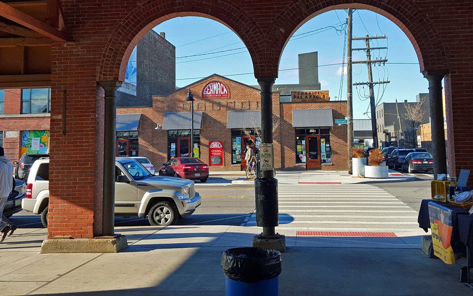 A view through a brick archway onto an Eastern Market street with shops and a mural