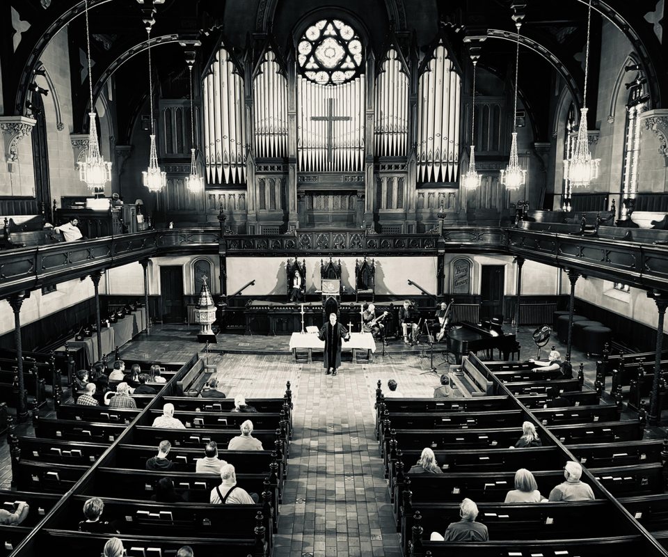 A black-and-white photo of the church's ornate interior with organ pipes and the congregation in the pews