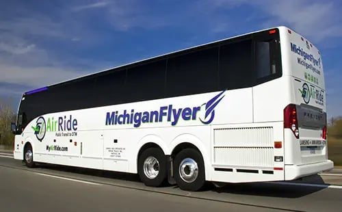 A white MichiganFlyer motorcoach drives along the highway