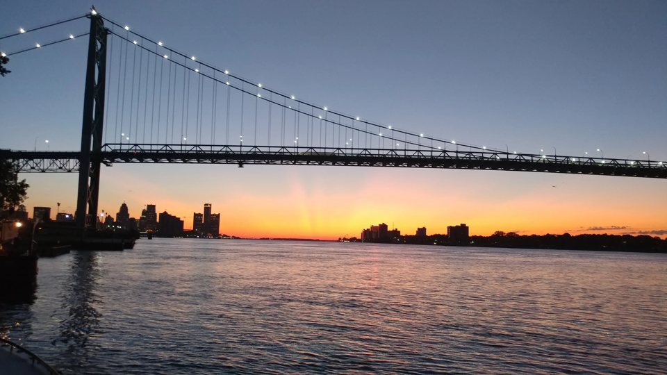 The Ambassador Bridge silhouetted at sunset, with Detroit's skyline glowing orange behind it