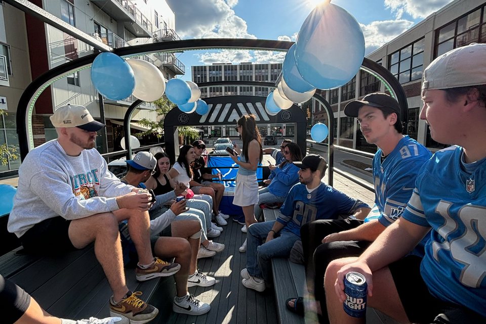 Passengers in Detroit Lions jerseys sit on the open-top bus with balloons during a daytime tour
