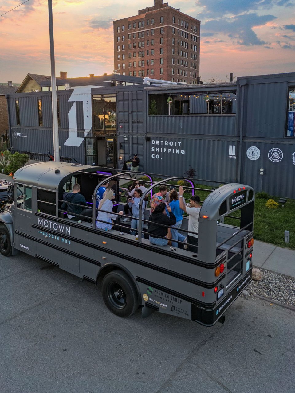 The Motown Boogie Bus parked at sunset in front of Detroit Shipping Co., with passengers aboard