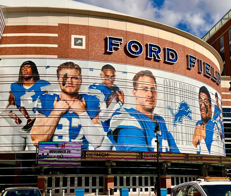Emberek pózolnak egy nagy falfestmény előtt, amely a Detroit Lions játékosait ábrázolja